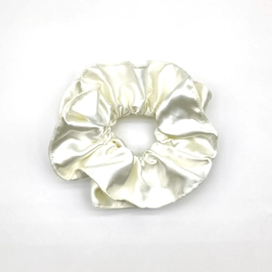 Macro detail of creamy white satin scrunchie with soft silk texture and elegant folds