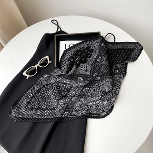 Detailed view of black and white paisley pleated scarf on a table with fashion accessories