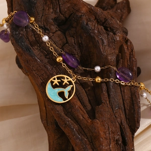 Macro detail of gold double-layer anklet with purple stones and whale tail pendant on wood