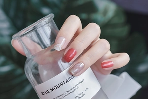 Detailed view of red and French tip manicured nails holding a glass bottle