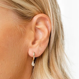 Close-up of gold hoop earring with clear teardrop gemstone pendant worn by a model