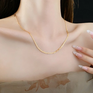 Close-up of flat gold chain necklace worn by a model against a black background
