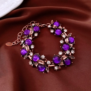 Detailansicht eines lila Perlenarmbandes mit roségoldenen Blumen und Strasssteinen.