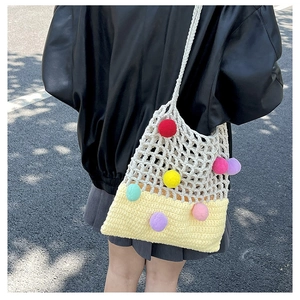 Close-up of a handmade knit tote bag with colorful pom-poms and contrast stitching