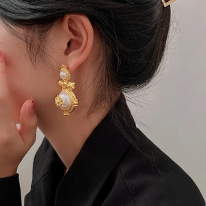 Baroque style gold flower earrings with large pearls worn by a model in a close-up detail