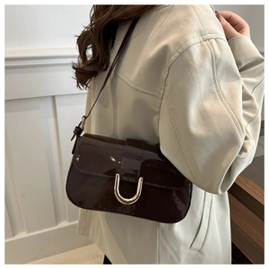 Detail of high-gloss chocolate brown patent leather bag with gold horseshoe buckle accent