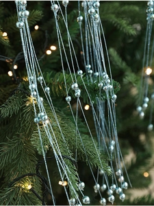 Gros plan d'une guirlande de perles bleu clair sur un sapin de Noël avec lumières chaudes