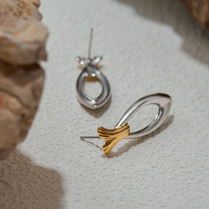 Macro shot of two-tone 18K stainless steel fish earrings on natural stone and sand background