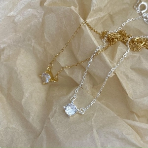 Detail of silver and gold solitaire necklaces with round zircon on textured paper