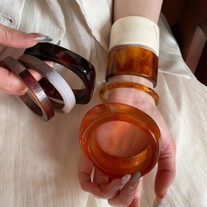 Close-up of retro iridescent resin bangles in amber and ivory tones worn by a model