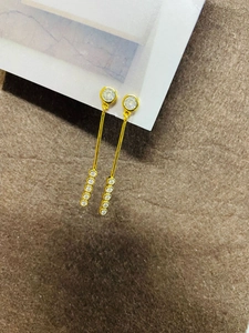 Détail de boucles d'oreilles pendantes dorées avec diamants sur carte blanche