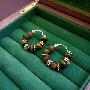 Detail of tiger eye beaded hoop earrings with gold-plated accents in green velvet box
