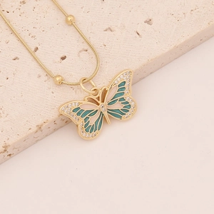 Elegant gold butterfly necklace with green and white enamel on beige stone surface