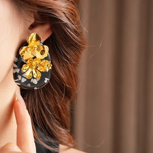 Close-up of vintage flower earrings with gold petals on black resin worn by a model