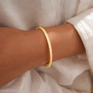 Detail of 18k gold plated geometric bangle with vertical texture on model's wrist