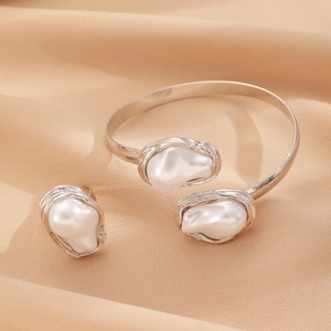 Detailed view of silver baroque pearl bracelet and open ring on champagne silk background