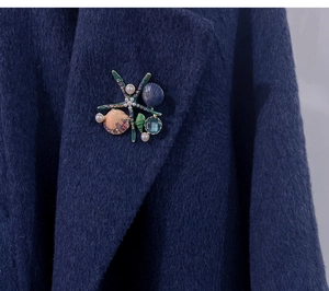 Macro detail of starfish and shell brooch with pearls and rhinestones on wool coat