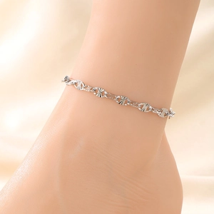 Detail of silver link anklet worn by a model on a beige silk background with soft lighting