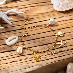 Golden ocean charm bracelet with shell, starfish, pearl and letter A on wood base