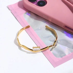 Détail du bracelet doré vague avec zircon rectangulaire sur fond rose iridescent