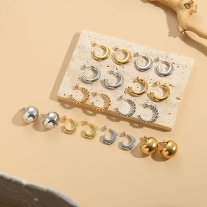 Collection of minimalist geometric gold and silver hoop earrings on natural stone display