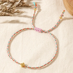 Macro shot of colorful braided rope bracelet with golden cross charm and adjustable cord