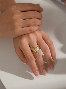 Detailed close-up of a wide golden hollow heart ring with a centered pearl on finger