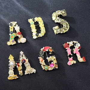 Detailed flat lay of vintage gold-tone letter brooches with pearls and colorful gems
