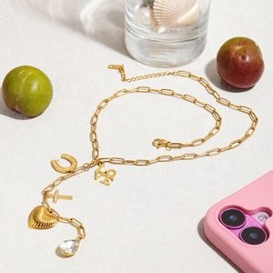 Collier à breloques doré avec fer à cheval, cœur et croix sur fond de sable