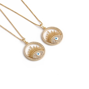 Détails de deux colliers dorés avec pendentifs soleil en zircon bleu et œil maléfique