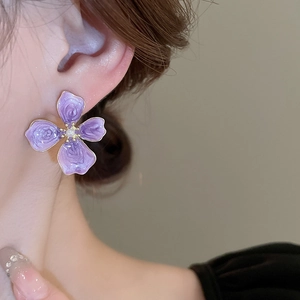 Detail of purple flower petal earring with pearl center worn by a model in warm light