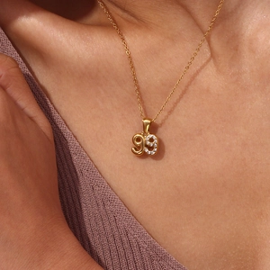 Close-up of gold number 99 pendant necklace with sparkling micro-pave zircons on a model