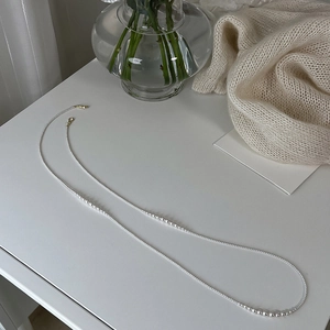 Detail view of long pearl necklace on a white desk with cream knit sweater background