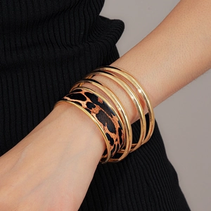 Gros plan de bracelets dorés empilés et manchette léopard sur le poignet d'une femme