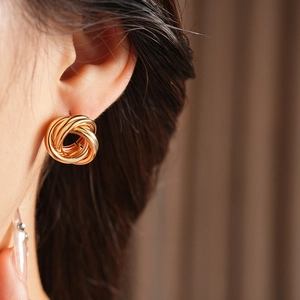 Gros plan de boucles d'oreilles nœud doré sur modèle, texture tissée et design torsadé
