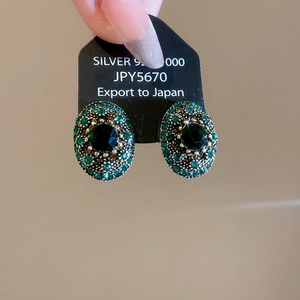 Detail of vintage oval earrings with deep green gemstones and silver pins on card