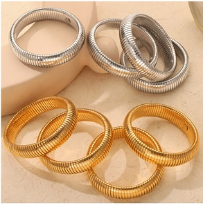 Close-up of stacked gold and silver spiral spring bangles with polished ribbed texture