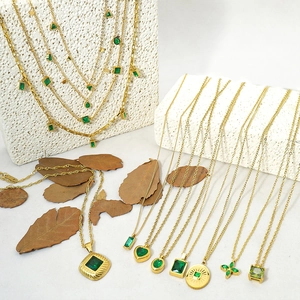 Detail of vintage gold necklaces with emerald green heart and clover pendants on stone