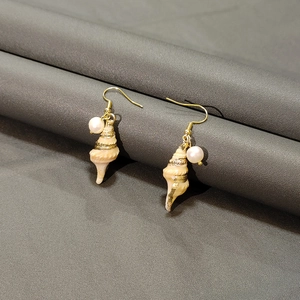 Close-up of golden seashell earrings with natural mother of pearl and white pearls