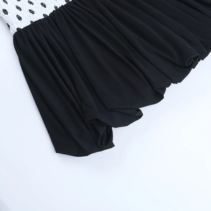 Close-up of contrast polka dot smocked bodice and pleated black fabric on V-neck dress