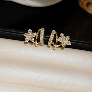 Elegant gold flower earrings with sparkling zircons on beige silk texture backdrop