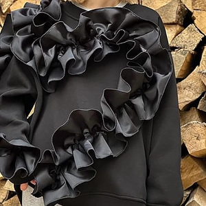Vue détaillée du sweat noir à manches longues avec de grands volants en satin décoratifs