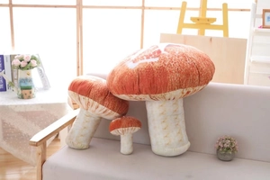Three sizes of realistic plush mushroom pillows on a cozy sofa in a bright home setting