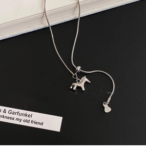 Detail of silver snake chain necklace featuring a horse pendant and dollar sign charm