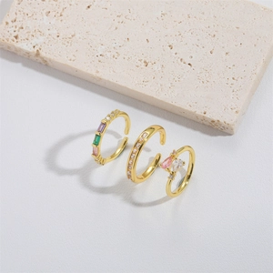 Three gold open rings with colorful gemstones and pearls on a beige textured stone base