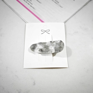 Detail of silver wavy metal hair clip with a brushed texture on a white card