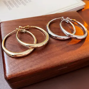Pair of minimalist gold and silver polished metal hoop earrings on a textured wooden base