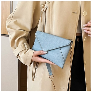 Close-up of light blue envelope crossbody bag with gold chain strap on trench coat