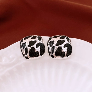 Macro detail of square silver stud earrings with black enamel spots on white ceramic tray