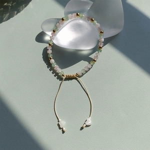 Close-up of handmade beaded bracelet with green and pink square stones and gold accents